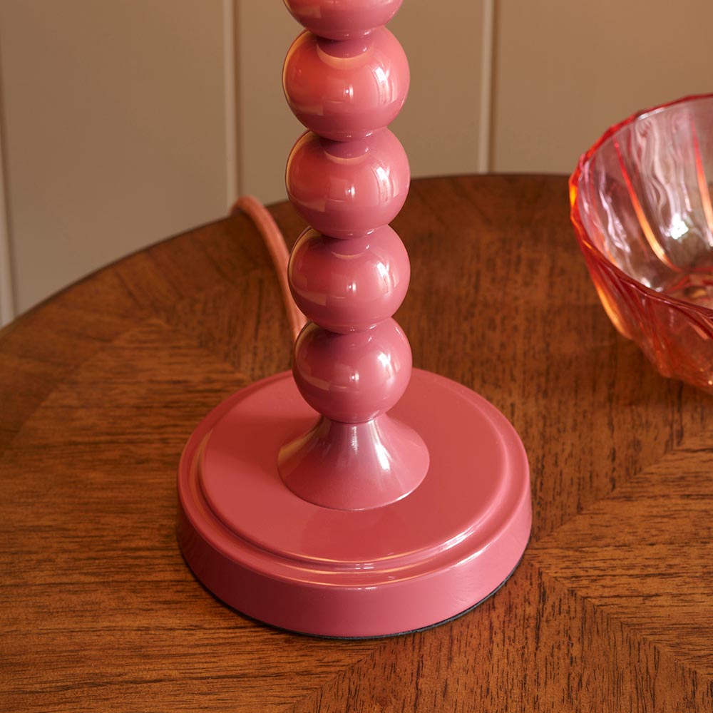 Close-up of the Brenleigh Zigzag Table Lamp's pink gloss stacked-sphere metal base with fabric flex, shown on a wooden table.