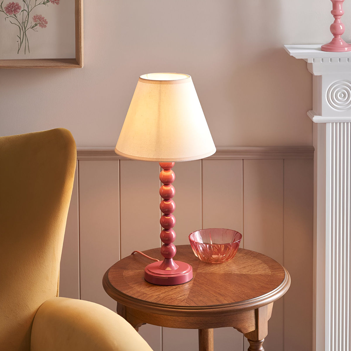 Endon Brenleigh Ivy table lamp with pink stacked-sphere metal base and vintage white tapered shade, on a wooden side table beside a mustard armchair.
