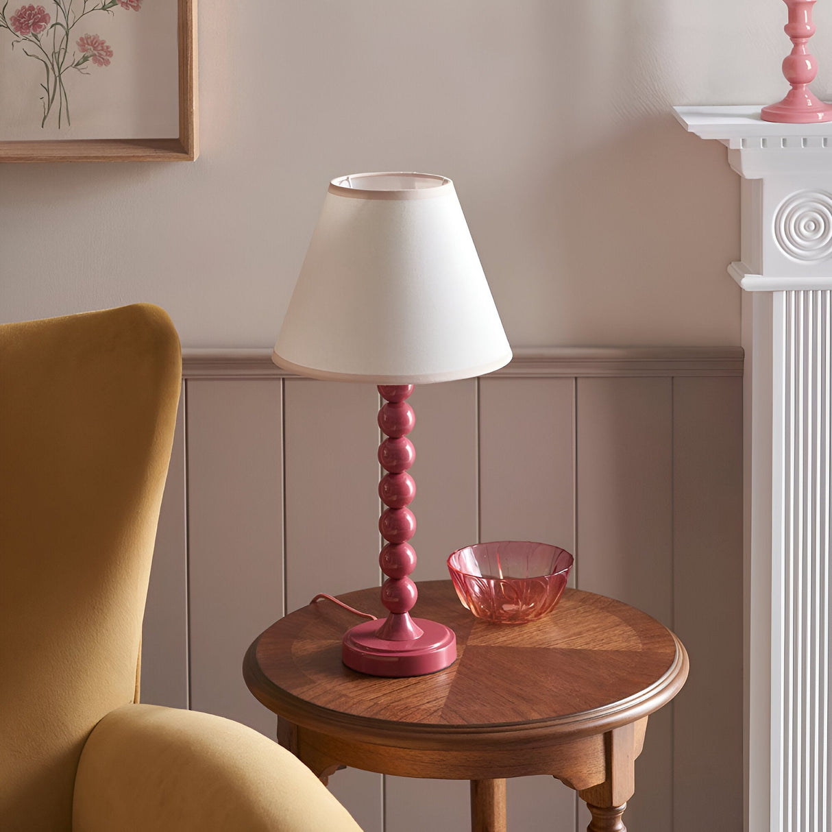 Endon Brenleigh Ivy table lamp with pink stacked-sphere metal base and white tapered shade, styled on a wooden side table beside a yellow armchair.