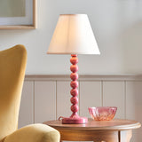 Endon Brenleigh Ivy table lamp with pink stacked-sphere metal base and white tapered fabric shade, on a wooden side table beside a pink glass bowl.