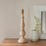Brenhurst Table Lamp base in natural turned wood with brass B22 bulb holder, unshaded, styled on a wooden surface beside a white jug and mirror.