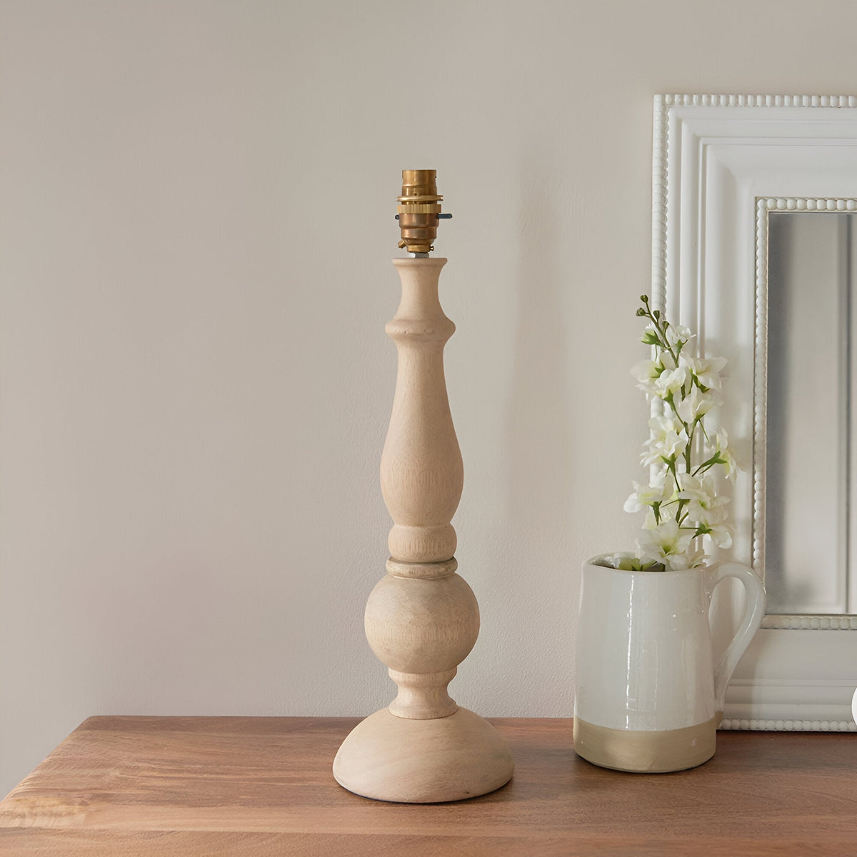 Brenhurst Table Lamp base in natural wood with turned column and brass B22 bulb holder, shown without shade on a wooden sideboard.