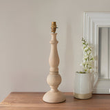 Brenhurst Table Lamp base in natural wood with turned column and brass B22 bulb holder, shown without shade on a wooden sideboard.