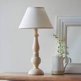 Brenhurst Table Lamp in Vintage White, hand-turned wood base with tapered cotton-mix shade, styled on a wooden surface beside a jug and flowers.