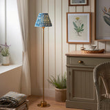 Endon Ashstead LED Ripple floor lamp with brushed brass stem and blue and white pleated shade, beside a green botanical print and grey cabinet.