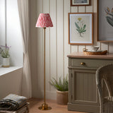 Endon Ashstead LED floor lamp with brushed brass stem and coral pink Ikat pleated shade, styled in a cottage-style living room beside a sideboard.