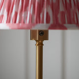 Close-up of Endon Ashstead LED floor lamp showing brushed brass stem, touch dimmer button and pleated coral pink Ikat fabric shade edge.