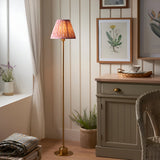 Endon Ashstead LED Ripple floor lamp on brushed brass stem with pink pleated Ripple shade, styled in a cottage-style living room beside a sideboard.