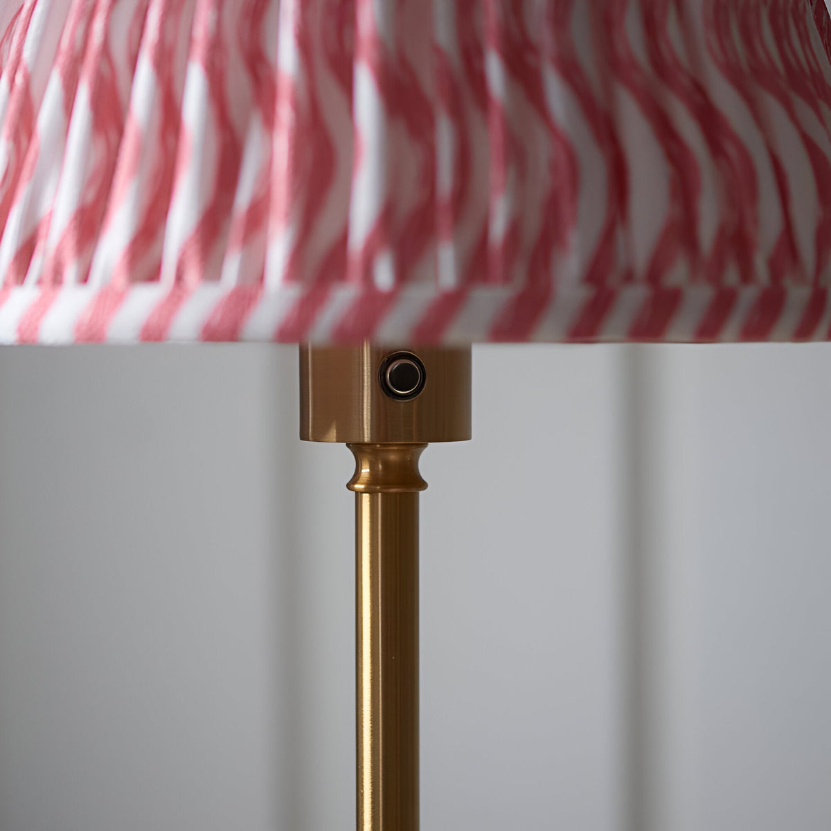 Close-up of the Endon Ashstead LED floor lamp's brushed brass stem and touch dimmer button beneath the pink and white Ripple pleated shade.