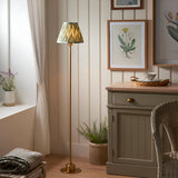 Endon Ashstead LED floor lamp with brushed brass stem and green zigzag pleated shade, placed in a cottage-style corner beside a sideboard and botanical prints.