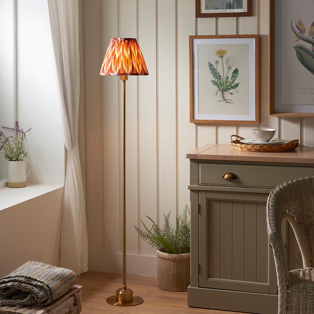 Endon Ashstead LED floor lamp with brushed brass stem and pleated apricot orange zigzag shade, styled beside a sage cabinet in a cottage living room.