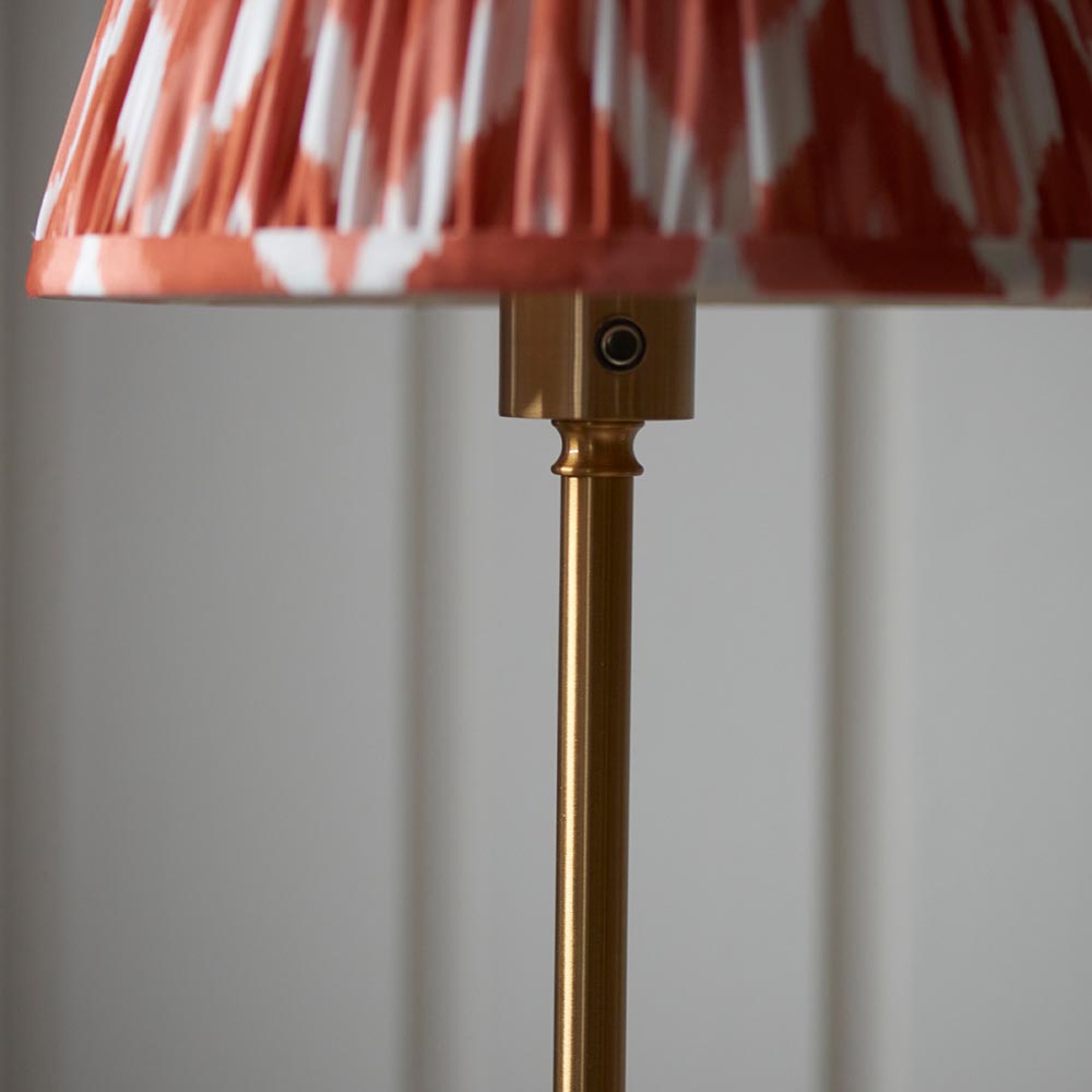 Close-up of the Endon Ashstead floor lamp's brushed aged brass stem and fitting beneath an apricot and white zigzag pleated fabric shade.