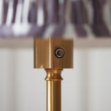 Close-up of the Endon Ashstead LED floor lamp's brushed brass stem and touch dimmer button, with the grey and white Ikat pleated shade above.