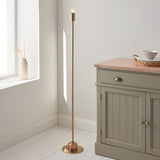 Endon Ashstead LED floor lamp in aged brass without shade, slim stem on a round base, shown beside a sage sideboard in a bright neutral room.