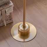 Close-up of the brushed aged brass round base of the Endon Ashstead LED Ivy floor lamp on wood flooring beside a wicker basket.