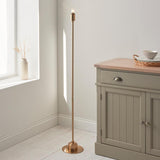 Endon Ashstead LED floor lamp on a slim brushed brass stem with round base and small bulb top, beside a sage sideboard and light window nook.