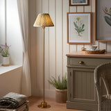 Endon Ashstead LED floor lamp with brushed brass stem and pleated green Leaf print shade, styled in a cottage-style living room beside a cabinet and window.