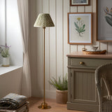Endon Ashstead LED floor lamp with brushed brass stem and green leaf-print pleated shade, in a cottage-style room with botanical prints and cabinet.