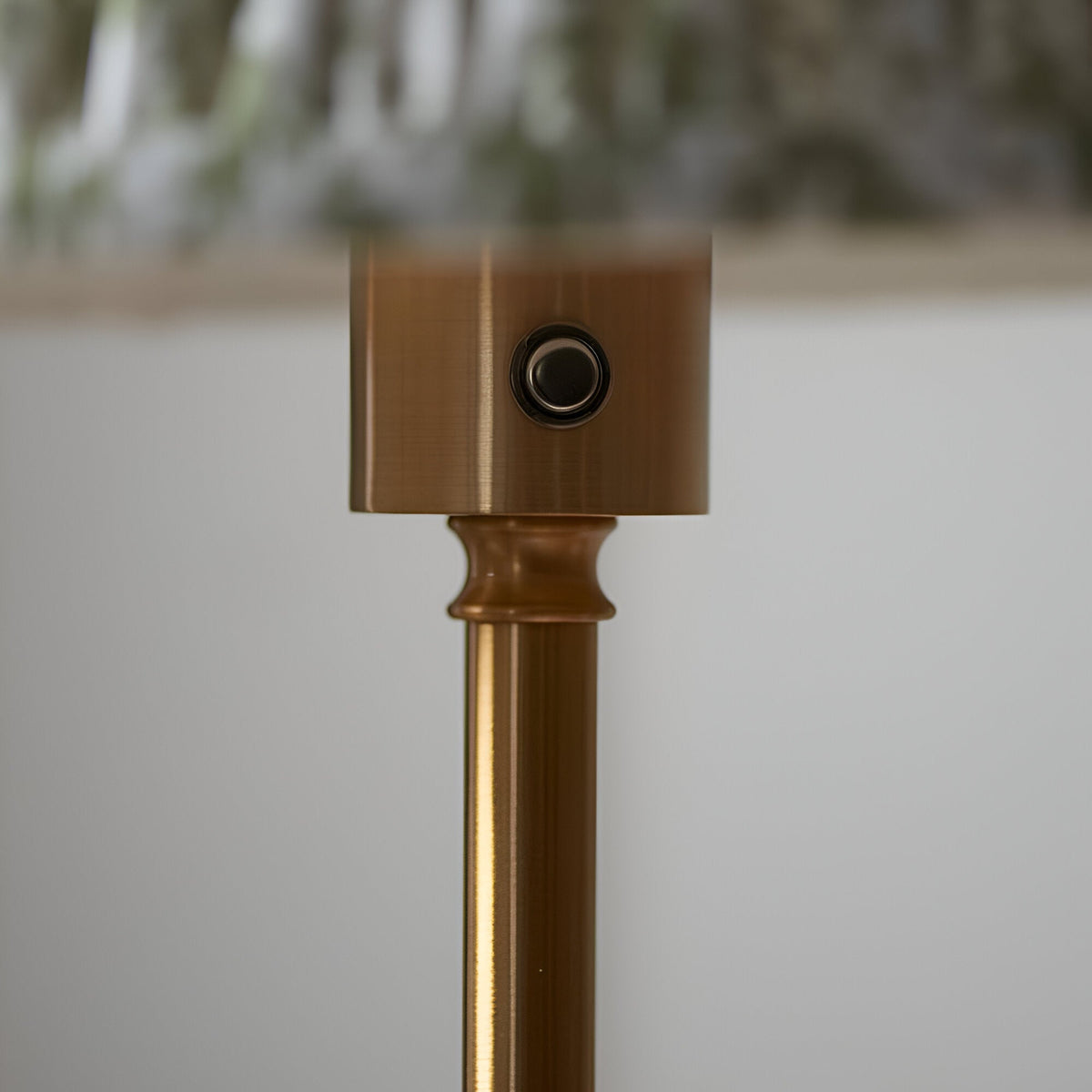 Close-up of the Endon Ashstead floor lamp's brushed aged brass stem, showing the cylindrical top housing with a small touch dimmer button.