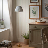 Ashstead LED Leaf Floor Lamp with brushed brass stem and pleated blue and white fabric shade, shown in a living room beside a sideboard.