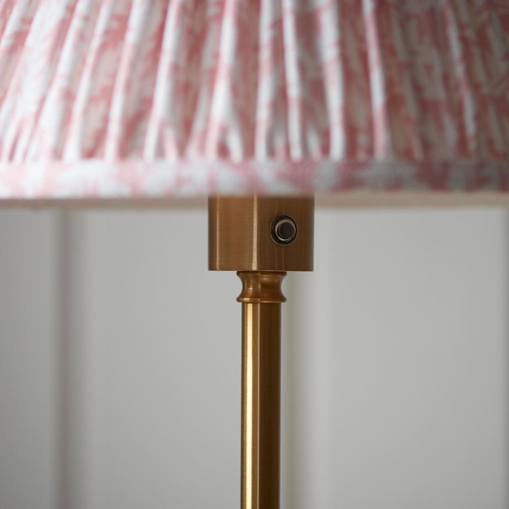 Close-up of the Ashstead LED Leaf Floor Lamp's brushed brass stem and switch beneath a pleated pink and white patterned fabric shade.