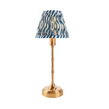 Ashstead LED table lamp with a slender brass stem, round base, and pleated blue, white, and gold ripple-patterned fabric shade, on a white background.