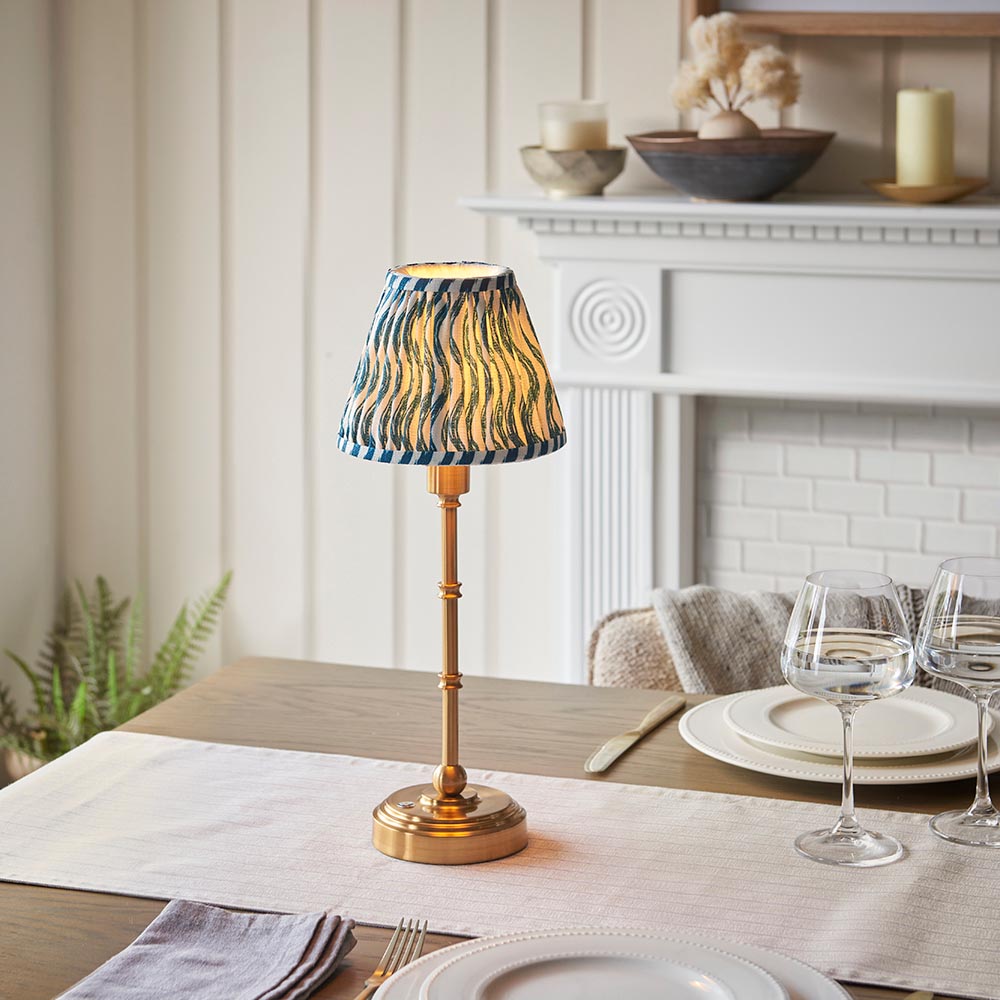 Ashstead LED Ripple Table Lamp with brass stem and base, blue and white patterned fabric shade, styled on a dining table near a white mantelpiece.