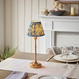 Ashstead LED Ripple Table Lamp with brass stem and base, blue and white patterned fabric shade, styled on a dining table near a white mantelpiece.