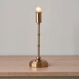 Ashstead LED table lamp with slim brass stem, round base, and exposed warm-white bulb, shown on a wooden surface against a plain background.