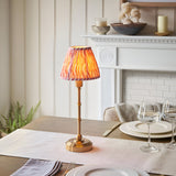 Endon Ashstead LED table lamp with brushed brass stem and pleated pink ripple-print shade, styled on a dining table beside a white fireplace.