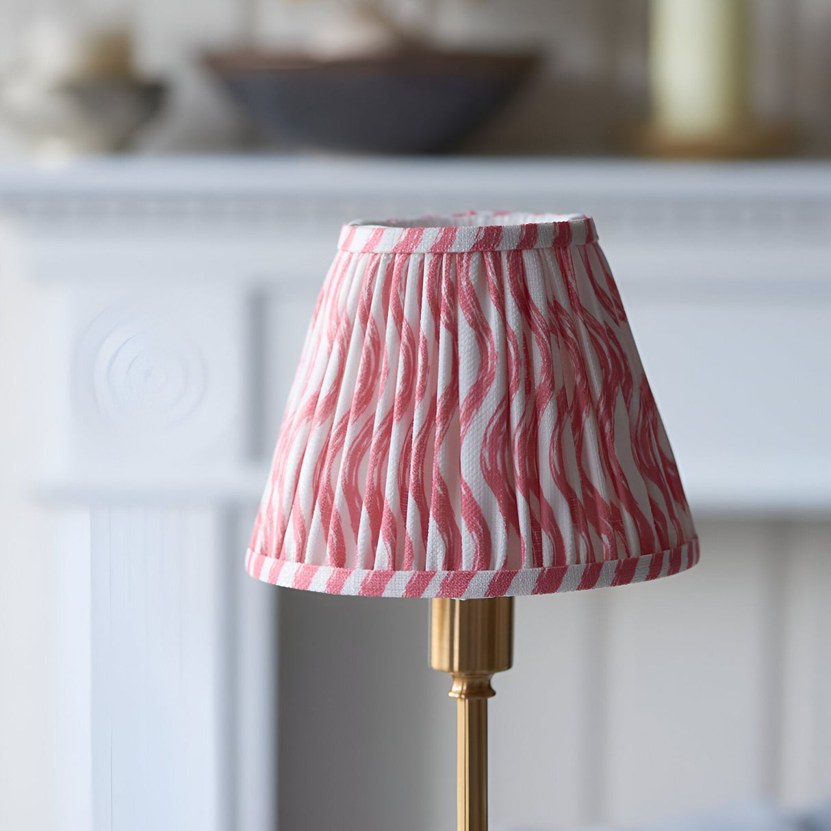 Endon Ashstead LED table lamp with a hand-pleated pink and white ripple-print fabric shade on a brushed brass stem, shown by a white fireplace mantel.