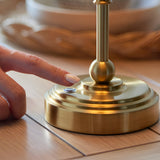 Finger touching the dimmer control on the brushed brass base of the Endon Ashstead Ripple LED table lamp on a wooden surface.