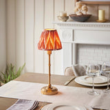 Endon Ashstead cordless LED table lamp with brushed brass stem and pleated apricot zigzag shade, set on a dining table beside wine glasses and plates.