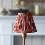 Endon Ashstead LED table lamp with brushed brass stem and handmade pleated zigzag shade in apricot orange and white, set before a pale mantelpiece.