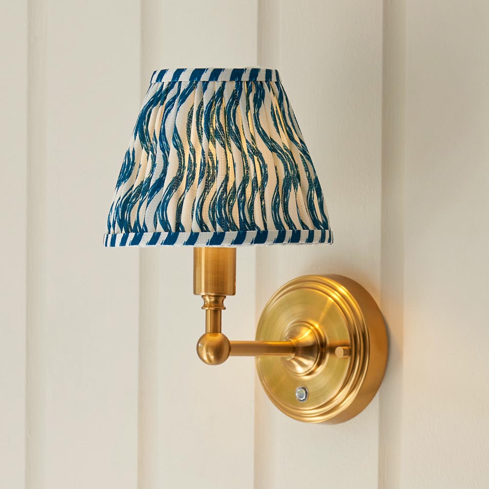Ashstead LED Ripple wall light with brushed brass arm and base, pleated blue and white patterned fabric shade, mounted on a light panelled wall.