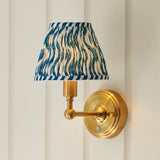 Ashstead LED Ripple wall light with brushed brass arm and base, pleated blue and white patterned fabric shade, mounted on a light panelled wall.