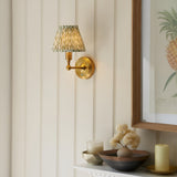 Endon Ashstead LED wall light with brushed brass arm and pleated green leaf-print shade, mounted on cream panelled wall beside a framed pineapple print.