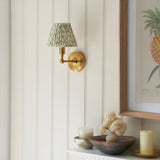 Endon Ashstead LED wall light with brushed brass arm and pleated green leaf-print shade, mounted on cream panelled wall beside a framed pineapple print.