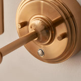 Close-up of the Endon Ashstead LED wall light's brushed aged brass wall plate, showing the arm fixing, knurled details and small charging port.