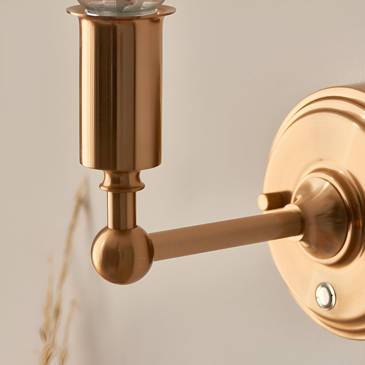 Close-up of Endon Ashstead LED wall light showing brushed aged brass arm, ball joint, cylindrical lamp holder and round wall plate.
