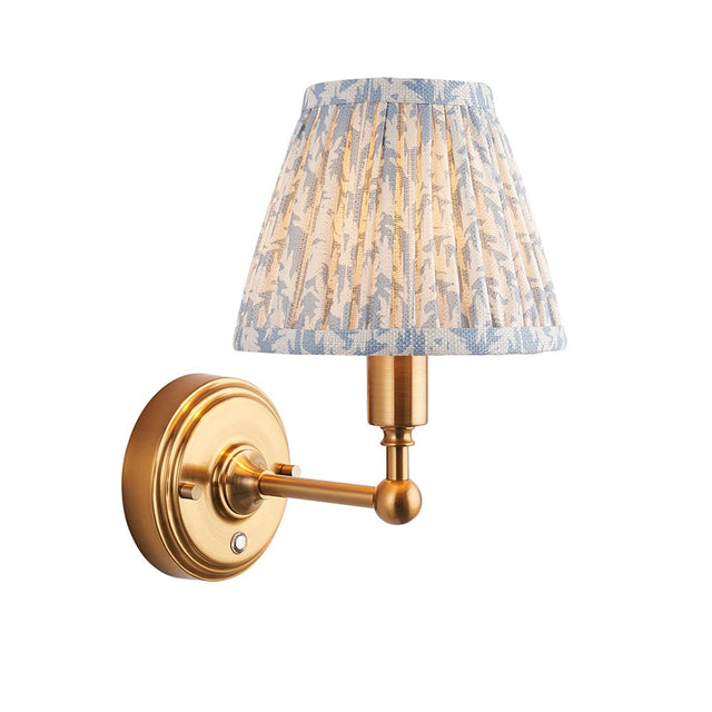 Endon Ashstead LED wall light with brushed brass arm and pleated blue and white leaf-print faux linen shade, on a plain white background.