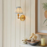 Endon Ashstead LED Leaf wall light with pleated blue and white faux linen shade on a brushed aged brass arm, mounted beside a botanical print.