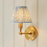 Endon Ashstead LED Leaf wall light with pleated blue and white faux linen shade on a brushed aged brass arm and round backplate, mounted on panelling.
