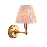 Ashstead LED wall light with pleated pink and white patterned fabric shade, brushed brass arm and round base, on a white background.