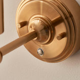 Close-up of the Ashstead LED Leaf Wall Light in brushed aged brass, showing the circular wall plate, arm, and push-button switch.