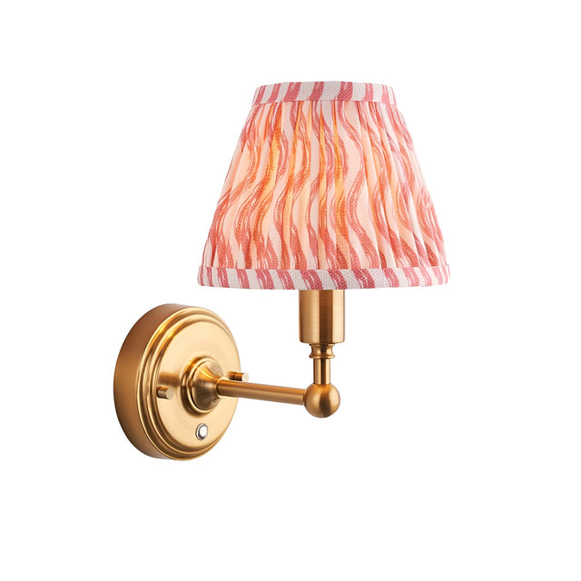 Endon Ashstead LED wall light with a pleated coral pink ripple-print faux linen shade on a brushed aged brass arm, shown on a white background.