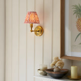Endon Ashstead LED wall light with brushed brass arm and pink ripple-print shade on a cream panelled wall beside a framed pineapple print.