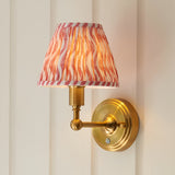 Endon Ashstead LED Ripple wall light with brushed brass arm and pleated coral pink and white patterned fabric shade, mounted on a cream panelled wall.
