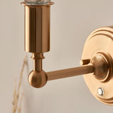 Close-up of Endon Ashstead LED Ripple wall light showing the brushed aged brass arm, ball joint, cylindrical bulb holder and round wall plate.