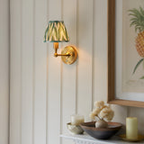 Endon Ashstead LED wall light in brushed brass with green and cream zigzag pleated shade, mounted on panelled wall beside framed pineapple print.